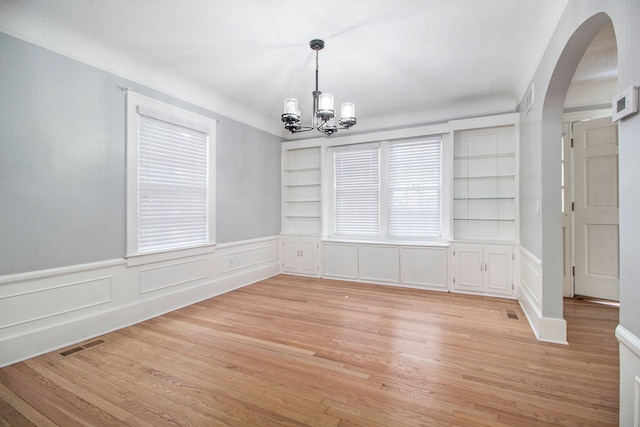 unfurnished dining area with built in shelves, light hardwood / wood-style floors, and an inviting chandelier