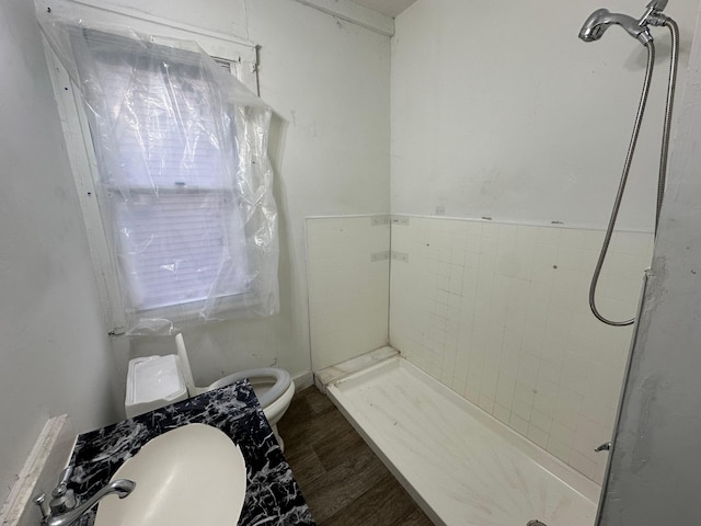 bathroom with tiled shower, wood-type flooring, and toilet