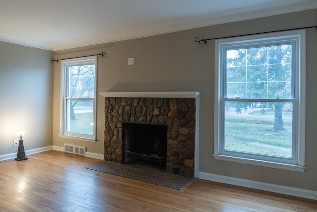 unfurnished living room featuring ornamental molding, a stone fireplace, and light hardwood / wood-style floors