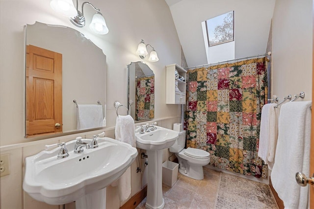 bathroom with tile patterned floors, toilet, lofted ceiling with skylight, and dual sinks