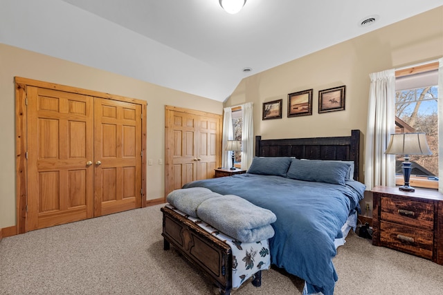 bedroom with two closets, light colored carpet, and lofted ceiling