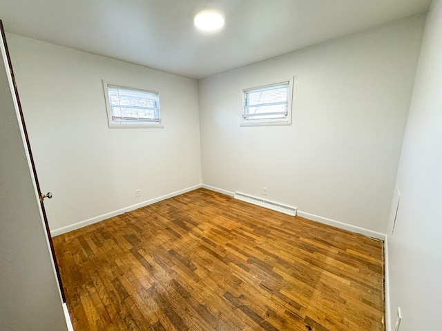 unfurnished room with plenty of natural light, a baseboard radiator, and wood-type flooring