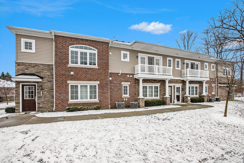 snow covered back of property featuring a balcony and central AC unit