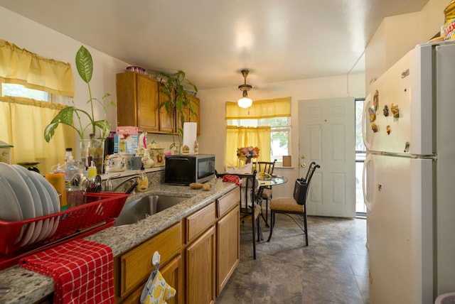 kitchen featuring white refrigerator, light stone counters, and sink