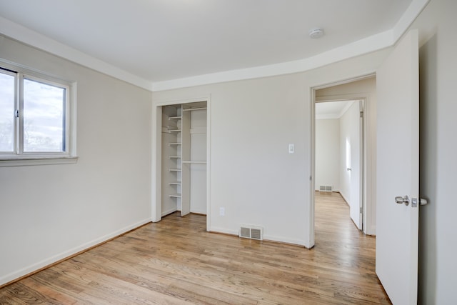 unfurnished bedroom with light wood-type flooring, crown molding, and a closet