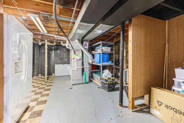 basement with wooden walls and white refrigerator with ice dispenser