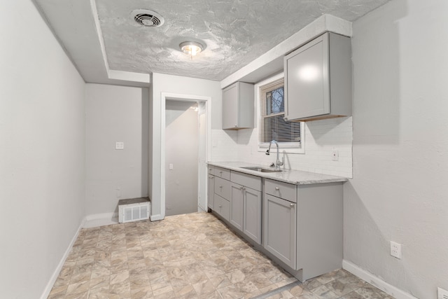 kitchen with a textured ceiling, gray cabinets, tasteful backsplash, and sink