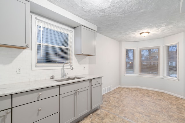 kitchen with a textured ceiling, gray cabinets, sink, and backsplash