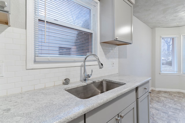 kitchen with gray cabinetry, light stone countertops, sink, and tasteful backsplash