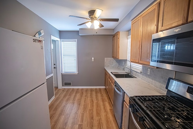 kitchen with sink, light hardwood / wood-style flooring, ceiling fan, appliances with stainless steel finishes, and backsplash