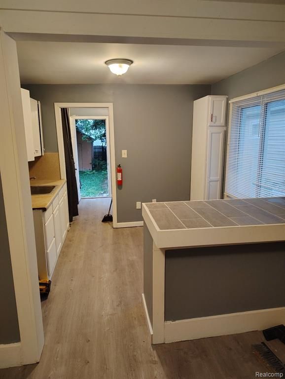 kitchen with tile countertops, white cabinetry, light hardwood / wood-style flooring, and sink