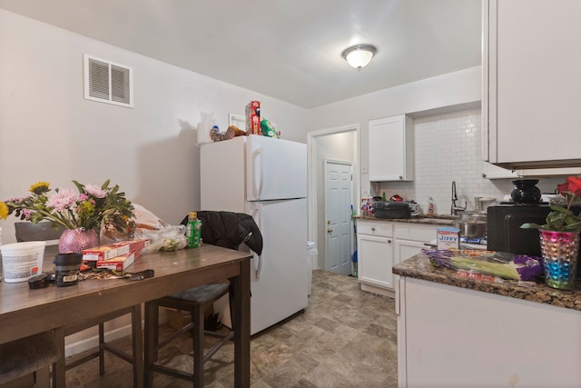 kitchen with dark stone counters, sink, decorative backsplash, white fridge, and white cabinetry