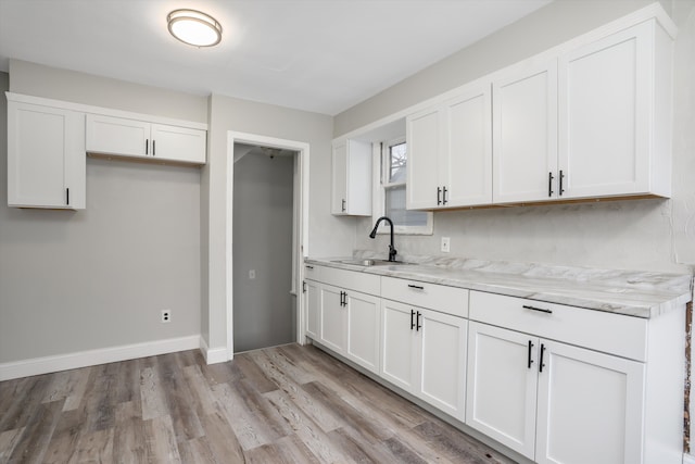 kitchen featuring white cabinets, light hardwood / wood-style floors, light stone counters, and sink