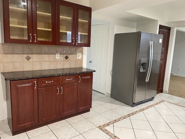 kitchen featuring decorative backsplash, stainless steel fridge with ice dispenser, dark stone countertops, and light tile patterned floors