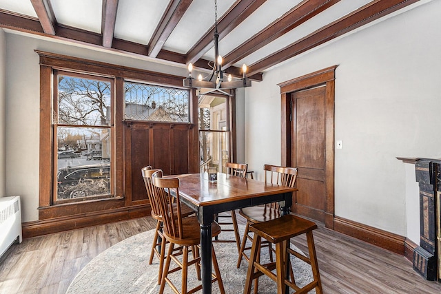 dining area featuring a chandelier, radiator heating unit, beamed ceiling, and light hardwood / wood-style floors