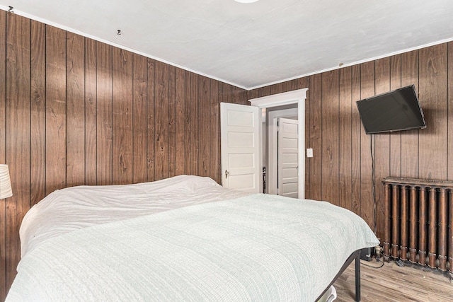 bedroom featuring light wood-type flooring, radiator heating unit, crown molding, and wooden walls