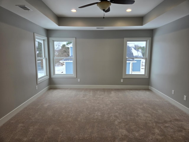 carpeted spare room with a raised ceiling and ceiling fan