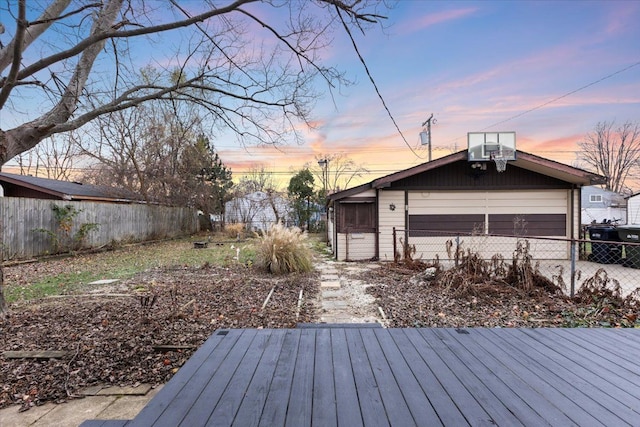 deck at dusk featuring a garage, an outdoor structure, and fence