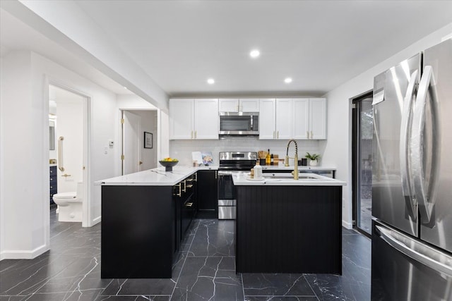 kitchen with a sink, appliances with stainless steel finishes, white cabinetry, dark cabinets, and backsplash