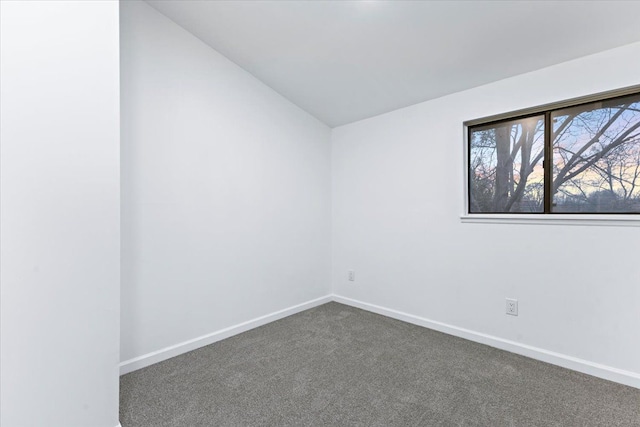 unfurnished room with dark carpet, baseboards, and vaulted ceiling