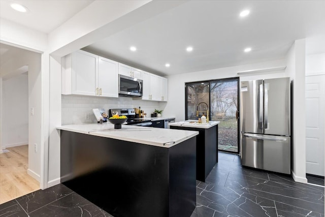 kitchen with marble finish floor, a center island with sink, backsplash, white cabinetry, and stainless steel appliances