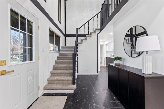 foyer featuring marble finish floor, a high ceiling, stairs, and baseboards