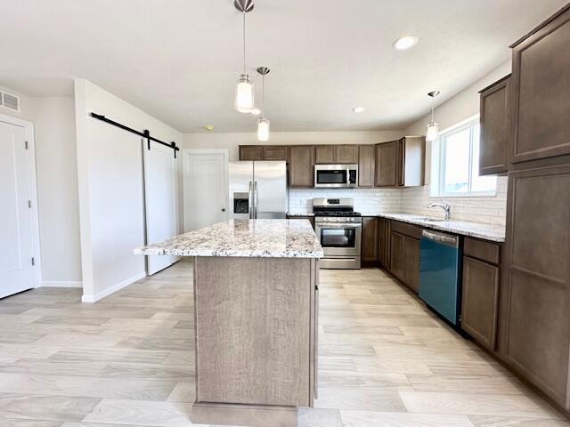 kitchen with a center island, decorative light fixtures, a barn door, and stainless steel appliances