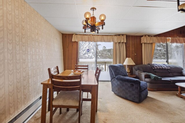 carpeted dining room featuring a paneled ceiling, a notable chandelier, wood walls, and a baseboard radiator