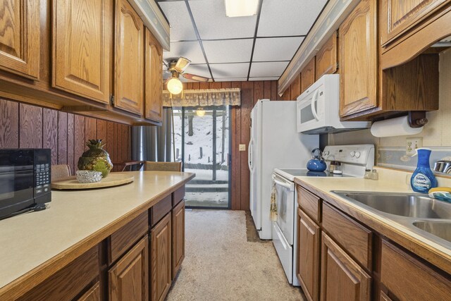 kitchen featuring sink, wooden walls, white appliances, a paneled ceiling, and light carpet