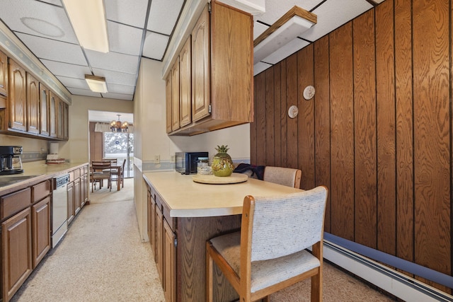 kitchen with dishwashing machine, a breakfast bar, baseboard heating, wooden walls, and an inviting chandelier