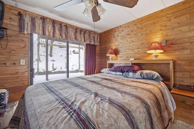 carpeted bedroom featuring access to exterior, ceiling fan, and wooden walls