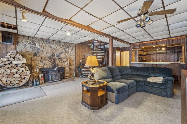 living room with carpet flooring, a paneled ceiling, a wood stove, and wooden walls