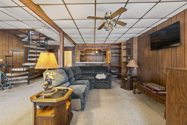 carpeted living room featuring a drop ceiling, ceiling fan, and wooden walls