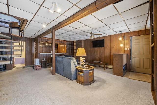 carpeted living room with ceiling fan, wood walls, and a drop ceiling