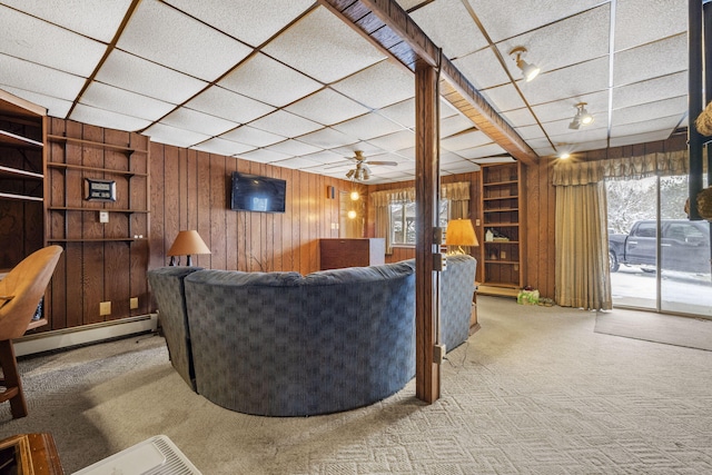 living room with ceiling fan, carpet floors, wooden walls, and a baseboard heating unit