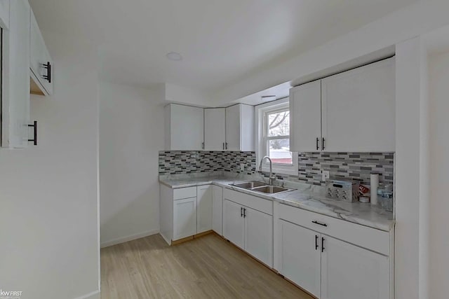 kitchen with white cabinets, light wood-type flooring, backsplash, and sink