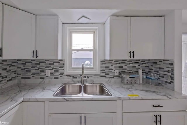 kitchen featuring decorative backsplash, white cabinetry, sink, and light stone countertops