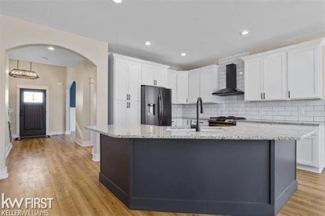 kitchen with wall chimney exhaust hood, light wood-type flooring, white cabinetry, and stainless steel refrigerator with ice dispenser