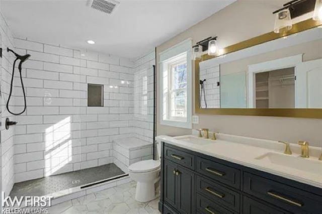 bathroom featuring a tile shower, vanity, and toilet