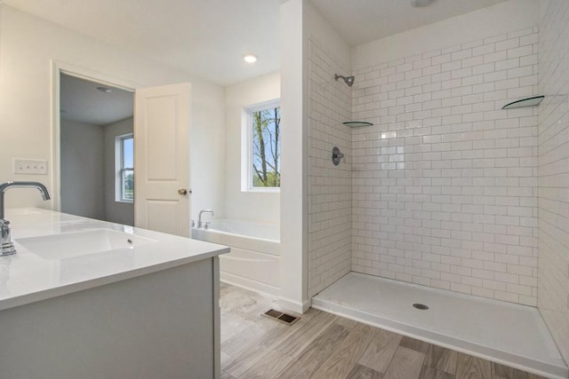 bathroom with wood finished floors, a sink, visible vents, tiled shower, and a bath