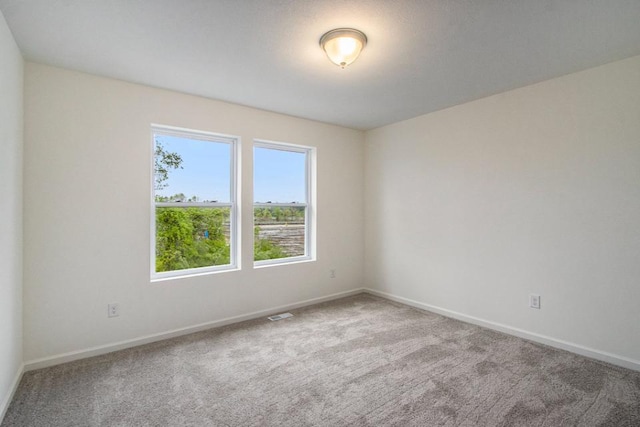 spare room featuring carpet, visible vents, and baseboards