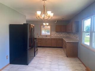 kitchen with black range oven, decorative backsplash, stainless steel fridge, decorative light fixtures, and a chandelier