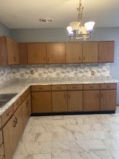 kitchen with decorative backsplash, sink, decorative light fixtures, and an inviting chandelier