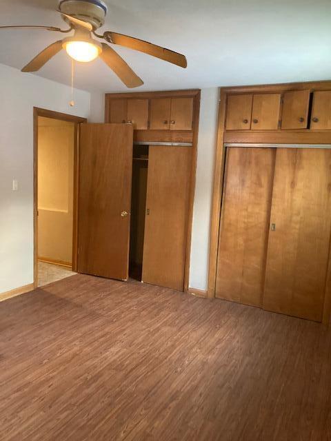 unfurnished bedroom featuring light wood-type flooring, ceiling fan, and multiple closets