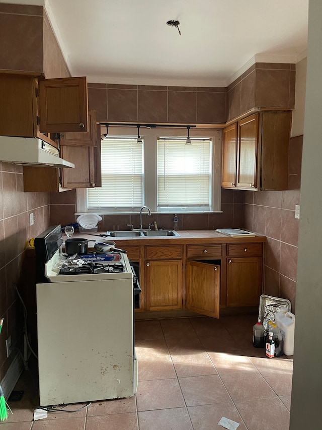 kitchen with sink, light tile patterned floors, tile walls, and white gas range oven