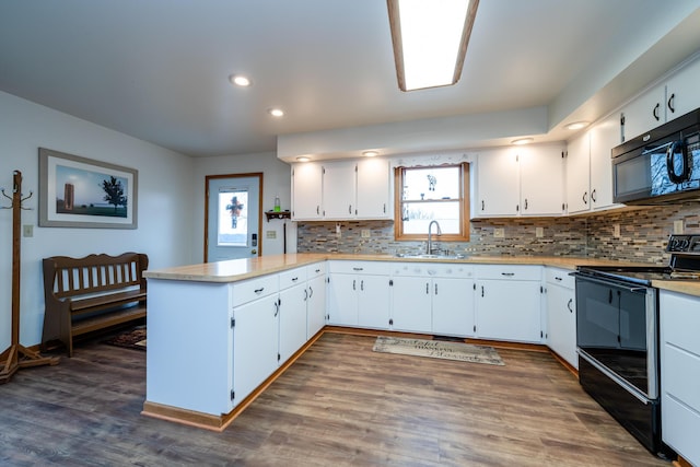 kitchen with sink, dark hardwood / wood-style floors, kitchen peninsula, white cabinets, and black appliances