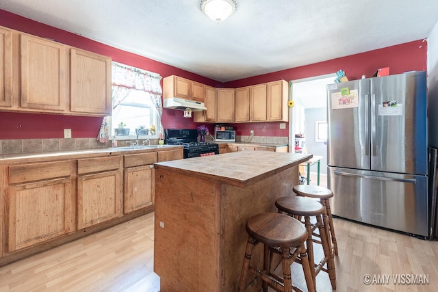 kitchen featuring stainless steel fridge, light wood-type flooring, sink, black gas stove, and a kitchen island