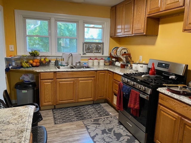 kitchen featuring light stone countertops, gas stove, light hardwood / wood-style flooring, and sink