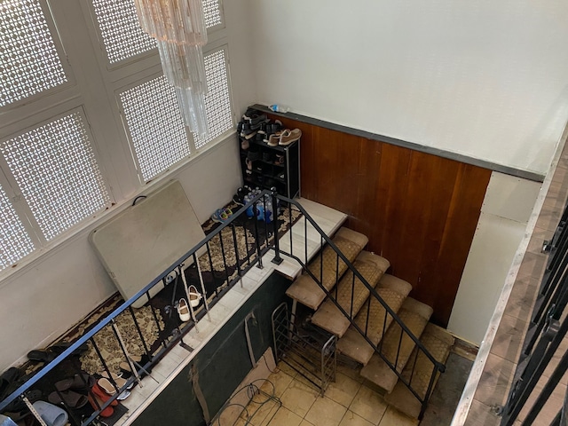 staircase featuring a healthy amount of sunlight, wooden walls, and a chandelier