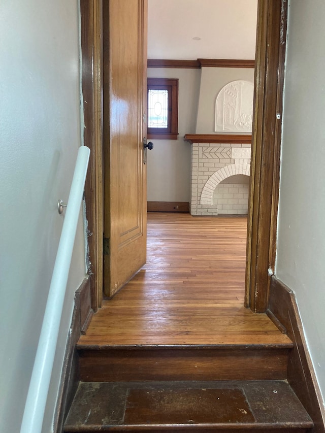 stairs with a fireplace, wood-type flooring, and crown molding